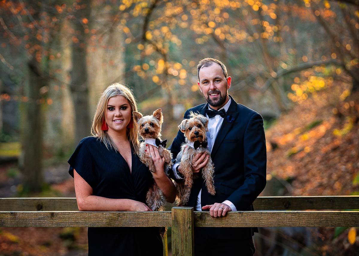Husband and Wife standing on a wooden bridge holding their Yorkshire Terriers for their photoshoot